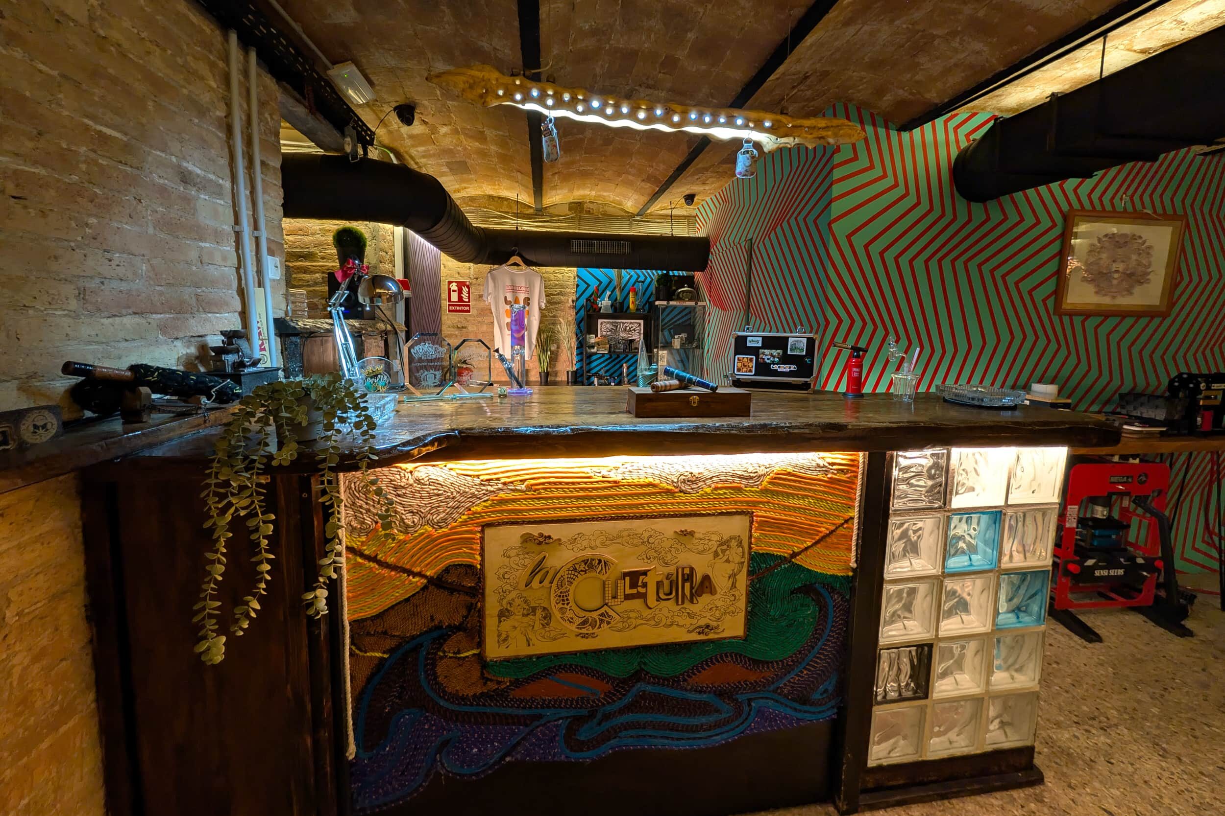 Area bar del club della cannabis La Cultura con bancone artistico e parete vivace a Barcellona
